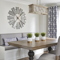 Custom-bench-seat-in-kitchen-with-wood-table-and-upholstered-gray-dining-room-chairs-and-plant-decor-and-round-clock-with-gold-pendant-and-custom-ripplefold-drapery-min