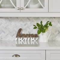 Home-decor-in-white-interior-kitchen-with-herrigbone-marble-backsplash-and-white-countertops-and-custom-cabinetry-with-green-plants-min