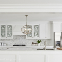 White-kitchen-with-pass-through-and-white-custom-cabinetry-with-round-endant-lighting-over-white-quartz-caountertop-and-stainless-steel-appliances-min
